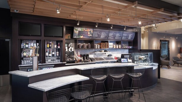 A modern bar area with a marble countertop, bar stools, and a menu board. - Courtyard by Marriott Baton Rouge Downtown (Baton Rouge)