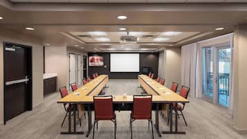 Un salón de conferencias con una larga mesa, sillas rojas, una pantalla de proyector y un amplio ventanal.