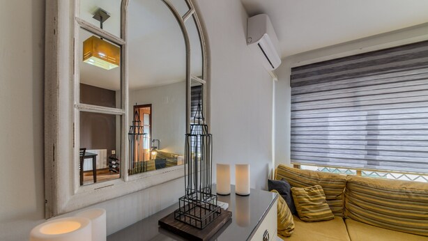 Een moderne woonkamer met een bank, een spiegel en een raam met zonwering.