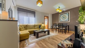 Een woonkamer met een bank, salontafel en een eethoek met stoelen.