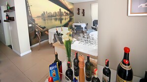 A dining area with a cityscape mural, a table set for a meal, and various bottles of wine. - Hotel Nika (Vlorë)