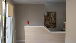 A reception area with a light-colored reception desk, a painting on the wall, and a window with blinds. - Hotel Nika (Vlorë)