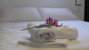 A neatly made bed with white linens, a rolled towel, and a bouquet of flowers on the bed. - Hotel Nika (Vlorë)
