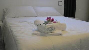 Un letto rifatto con cura, un asciugamano arrotolato e un bouquet di fiori sopra.