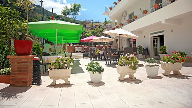 An outdoor patio area with tables and chairs, potted plants, and umbrellas. - Hotel Nika (Vlorë)