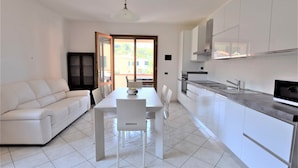 A modern kitchen with white cabinets, a dining table, and chairs. There is a sofa and a TV in the living area. - Holiday Apartment Ciliegio, Marina di Campo convenient for the beach and center. (Marina di Campo)