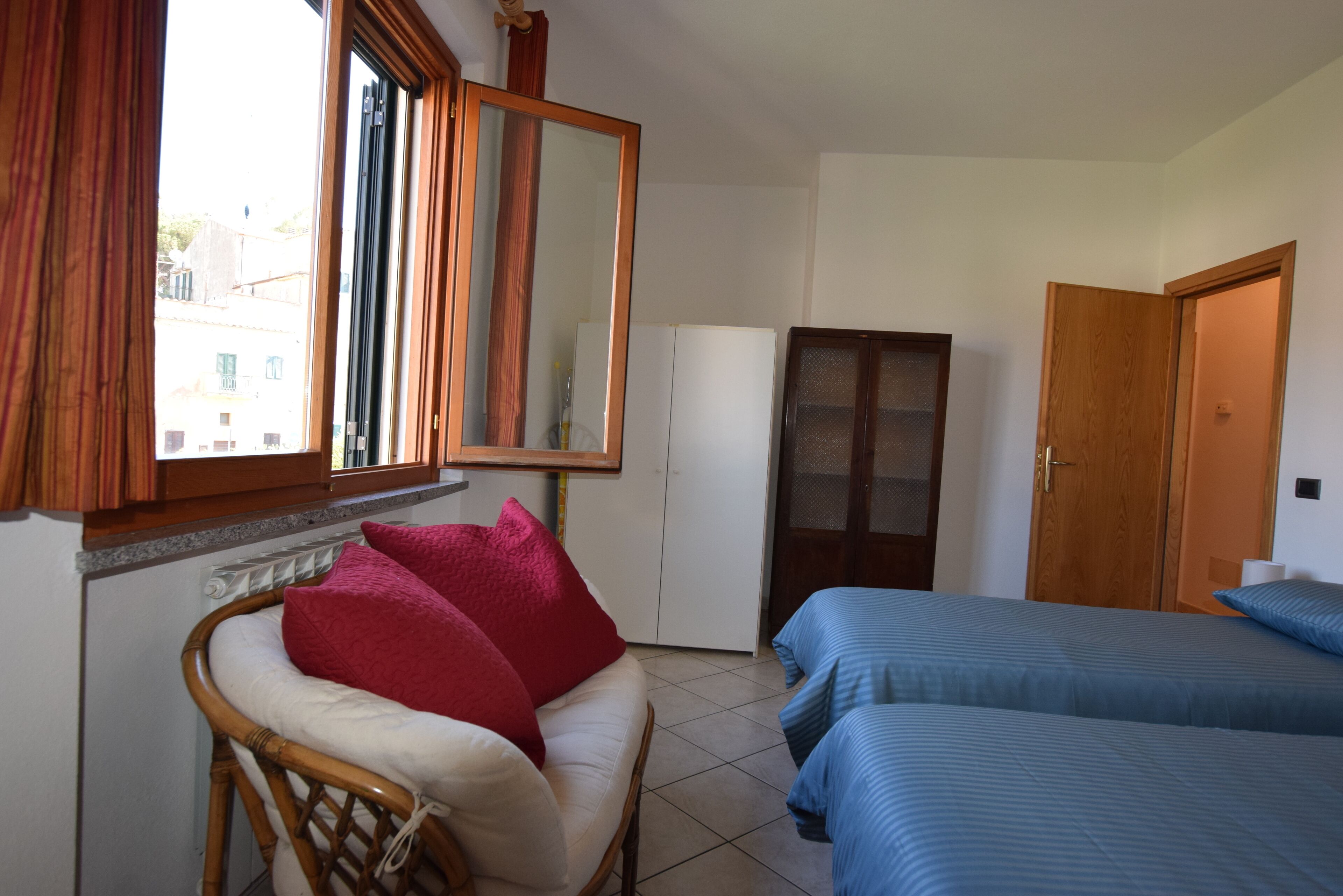 A room with a bed, a chair with cushions, a mirror, and a wardrobe.