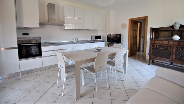 A modern kitchen with white cabinets, a dining table with chairs, a built-in oven, and a television. - Holiday Apartment Ciliegio, Marina di Campo convenient for the beach and center. (Marina di Campo)