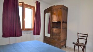 A bedroom with a bed, a wooden wardrobe, a chair, and a window with curtains. - Holiday Apartment Ciliegio, Marina di Campo convenient for the beach and center. (Marina di Campo)