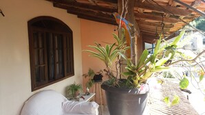 A balcony with a potted plant, a wooden chair, and a window with wooden shutters. - Casa de Maria (Angra dos Reis)