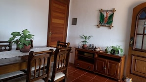 A dining area with a wooden table and chairs, a wooden cabinet with plants, and a door with a textured wall. - Casa de Maria (Angra dos Reis)