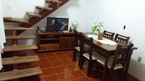 A dining area with a wooden table, chairs, and a television on a wooden stand. - Casa de Maria (Angra dos Reis)