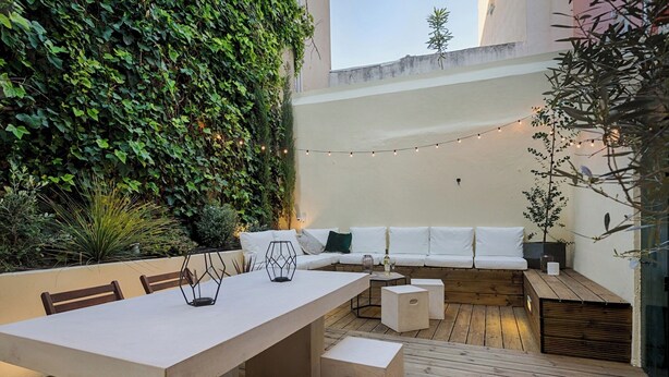 Une terrasse extérieure avec une longue table, des bancs, un canapé et des guirlandes lumineuses.
