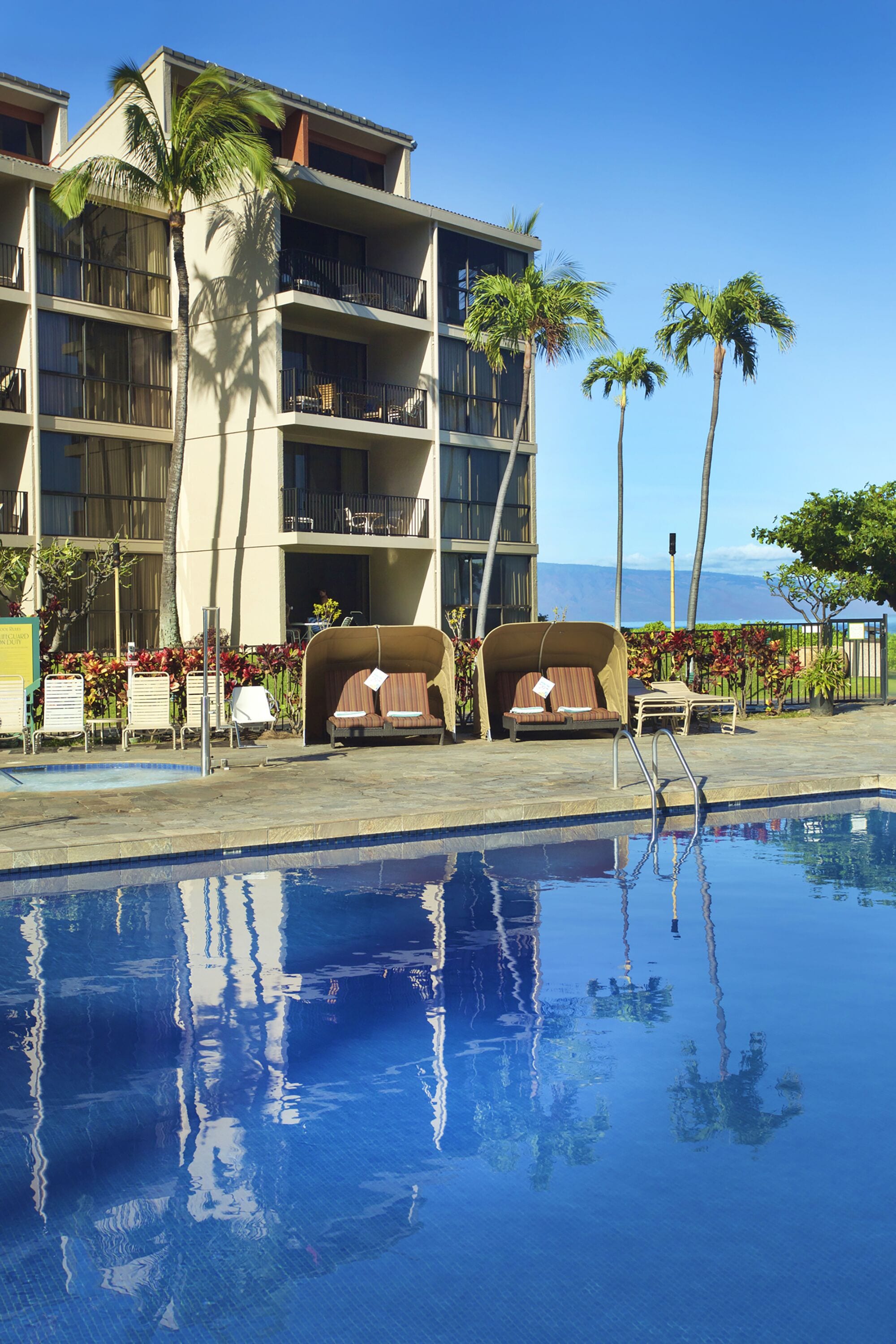 A hotel with a pool, lounge chairs, and palm trees.
