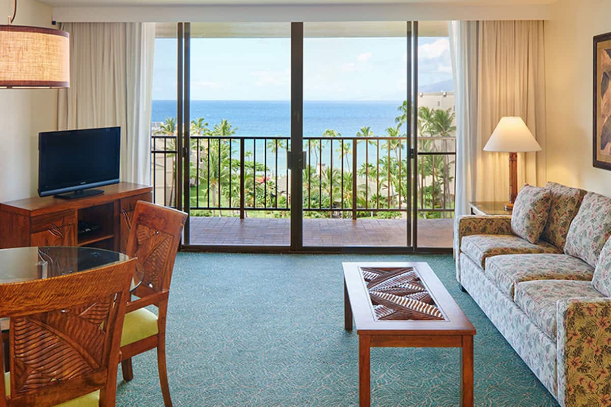 Ein Hotelzimmer mit Fernseher, einer Couch, einem Esstisch und Meerblick durch eine Schiebetür.