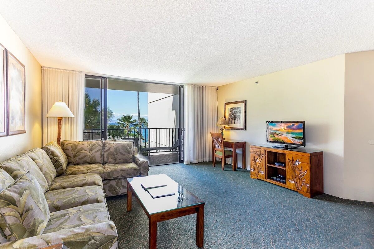 A living room with a sofa, a coffee table, a TV, and a balcony with curtains.