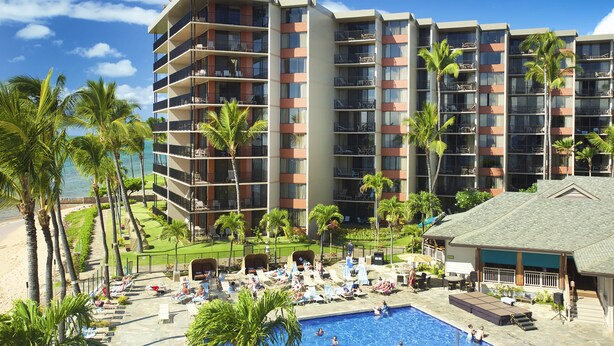 Un hotel con varios pisos, piscina exterior y palmeras.