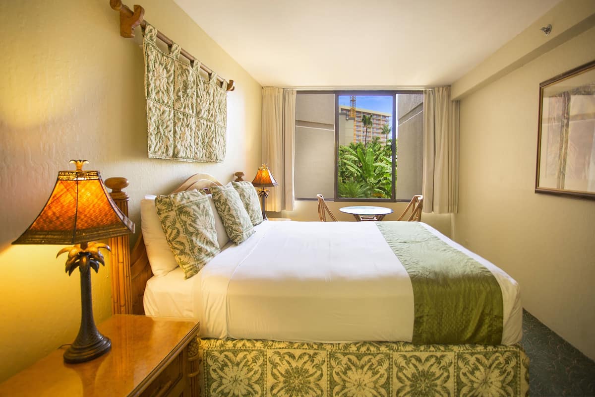 Ein Hotelzimmer mit Bett, zwei Nachttischlampen, einem kleinen Tisch und Blick nach außen.