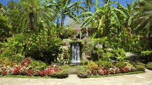 Un exuberante jardín con cascada, plantas tropicales y un pabellón.