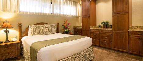Un dormitorio con una cama grande, armarios de madera, una mesita de noche con lámpara y una ventana con cortinas.