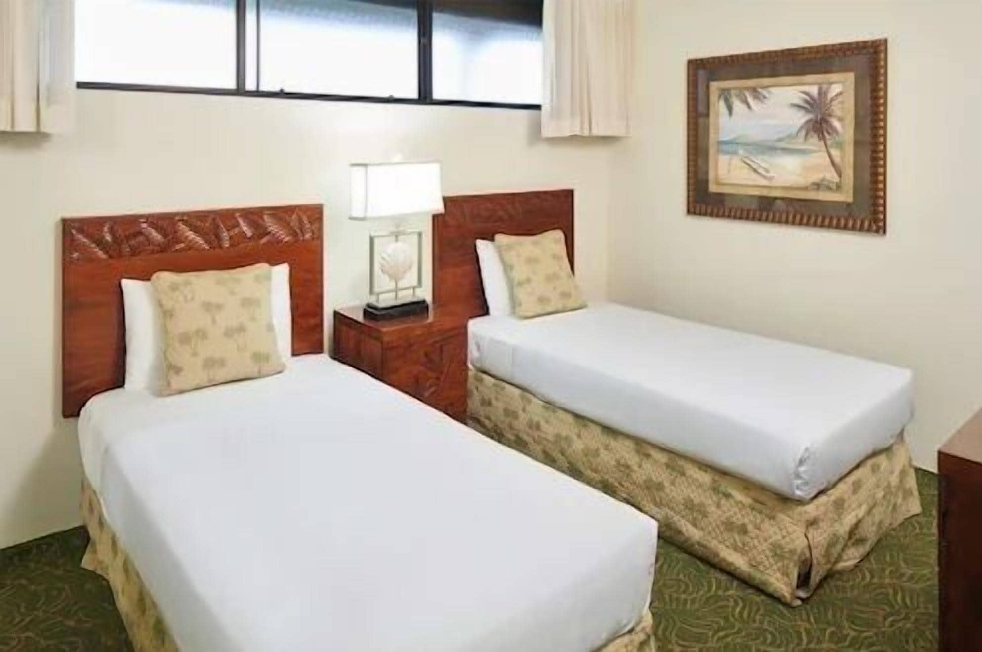 Two single beds with wooden headboards, a nightstand with a lamp, and a framed picture on the wall.