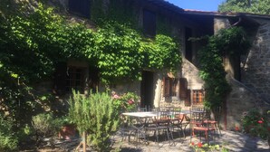 Une cour bordée de murs en pierre, avec une table, des chaises et des plantes en pot.
