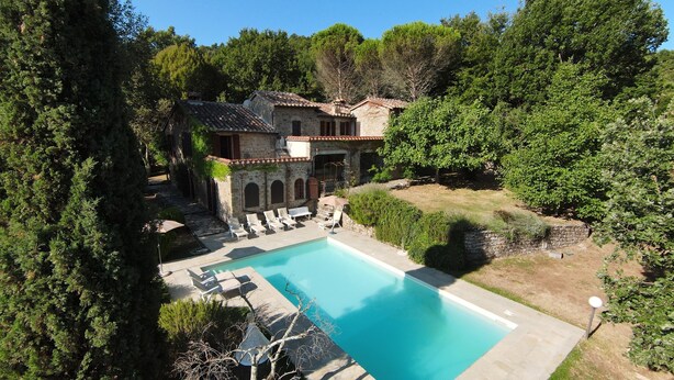 Une villa en pierre dotée d’une piscine, entourée d’une végétation luxuriante et d’arbres.