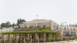 A building with a white facade, stone columns, and a flag. - Eliofos Elegant Maisonettes (Polis)