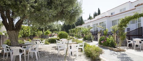 An outdoor patio area with white plastic chairs and tables, surrounded by gravel and small plants.