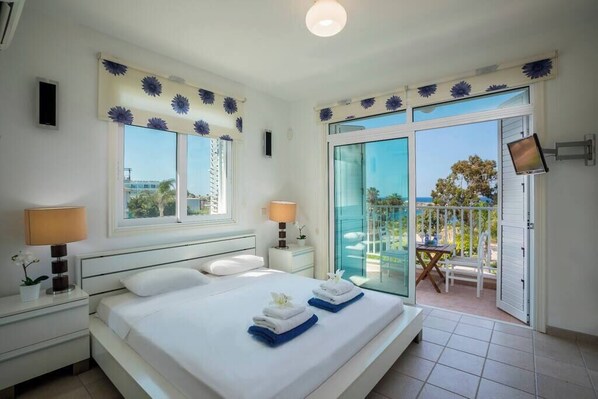 A hotel room with a bed, two bedside tables, a TV, and a balcony with a table and chairs.