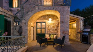 An outdoor patio with stone walls, a wooden grill, and wicker furniture.