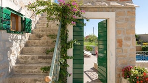 A stone staircase leading to a doorway with green shutters, surrounded by flowering plants.