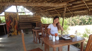 A wooden dining table with chairs, a painting on the wall, and a person seated. - Sigiriya vista (Avudangawa)