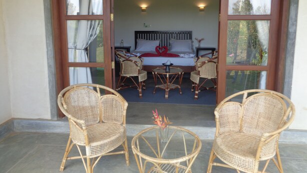 A room with a bed, two wicker chairs, a small table, and a view of the outdoors. - Sigiriya vista (Avudangawa)