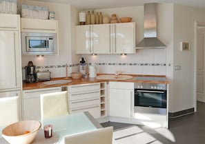 Une cuisine moderne avec des meubles blancs, un four à micro-ondes, une cuisinière et un évier. On y trouve des chaises et une table avec un bol et une tasse.