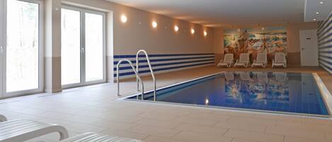 An indoor swimming pool with a tiled floor, a pool ladder, and several lounge chairs.