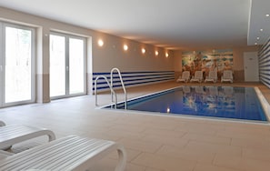 Ein Hallenbad mit Fliesenboden, einer Poolleiter und mehreren Liegestühlen.