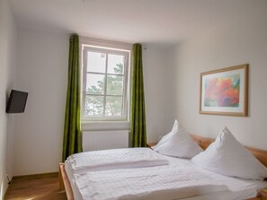 Un dormitorio con cama, ventana con cortinas, radiador y un cuadro en la pared.
