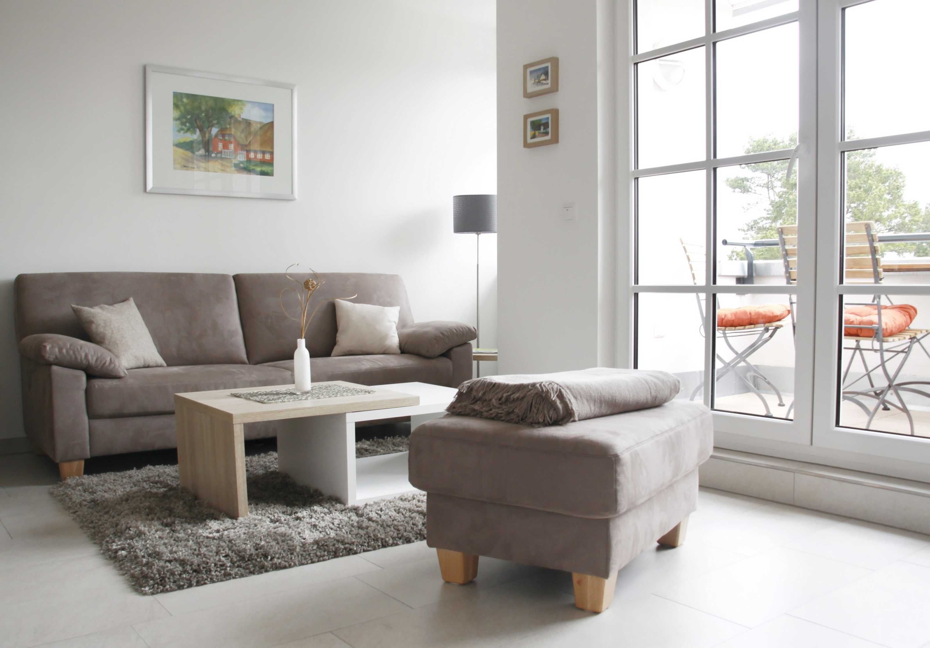 Un salon moderne avec un canapé, un pouf, une table basse et une grande fenêtre donnant sur un beau paysage.