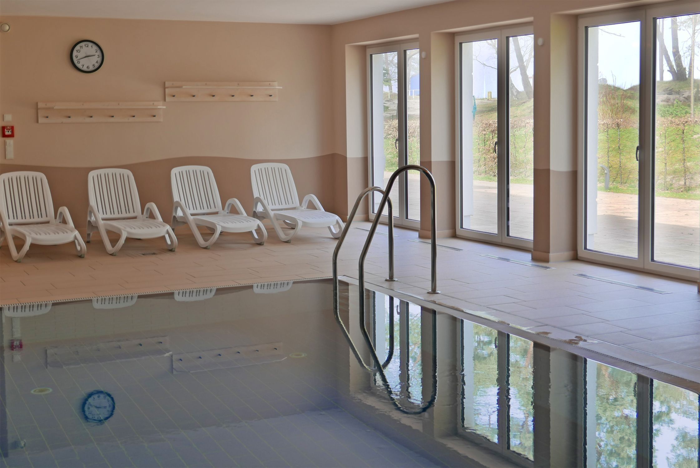 An indoor swimming pool with white lounge chairs and a clock on the wall.