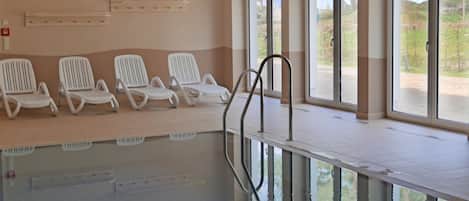 Una piscina interior con sillas reclinables blancas y un reloj en la pared.