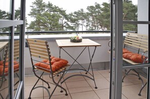 Ein Balkon mit Tisch und zwei Stühlen, einer davon mit orangefarbenem Kissen.