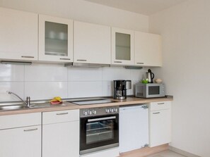Una cocina moderna con gabinetes blancos, un lavamanos de acero inoxidable, una cafetera, un microondas y un horno.