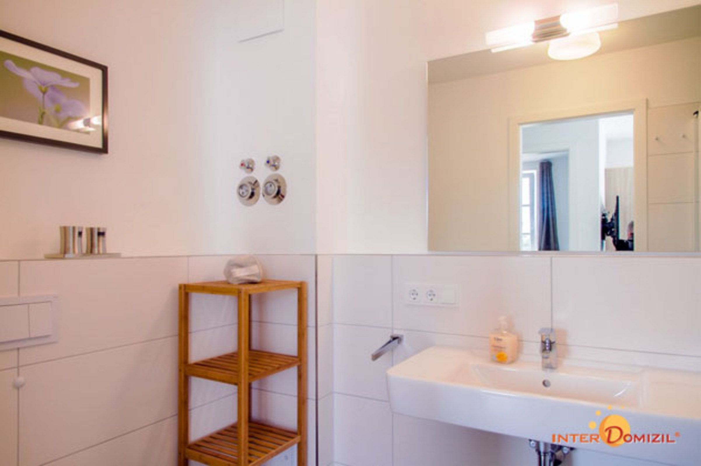 Ein Badezimmer mit einem weißen Waschbecken, einem Spiegel und einem Holzregal.
