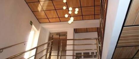 Un interior moderno con techo de madera, una escalera con barandillas de vidrio y una lámpara colgante.
