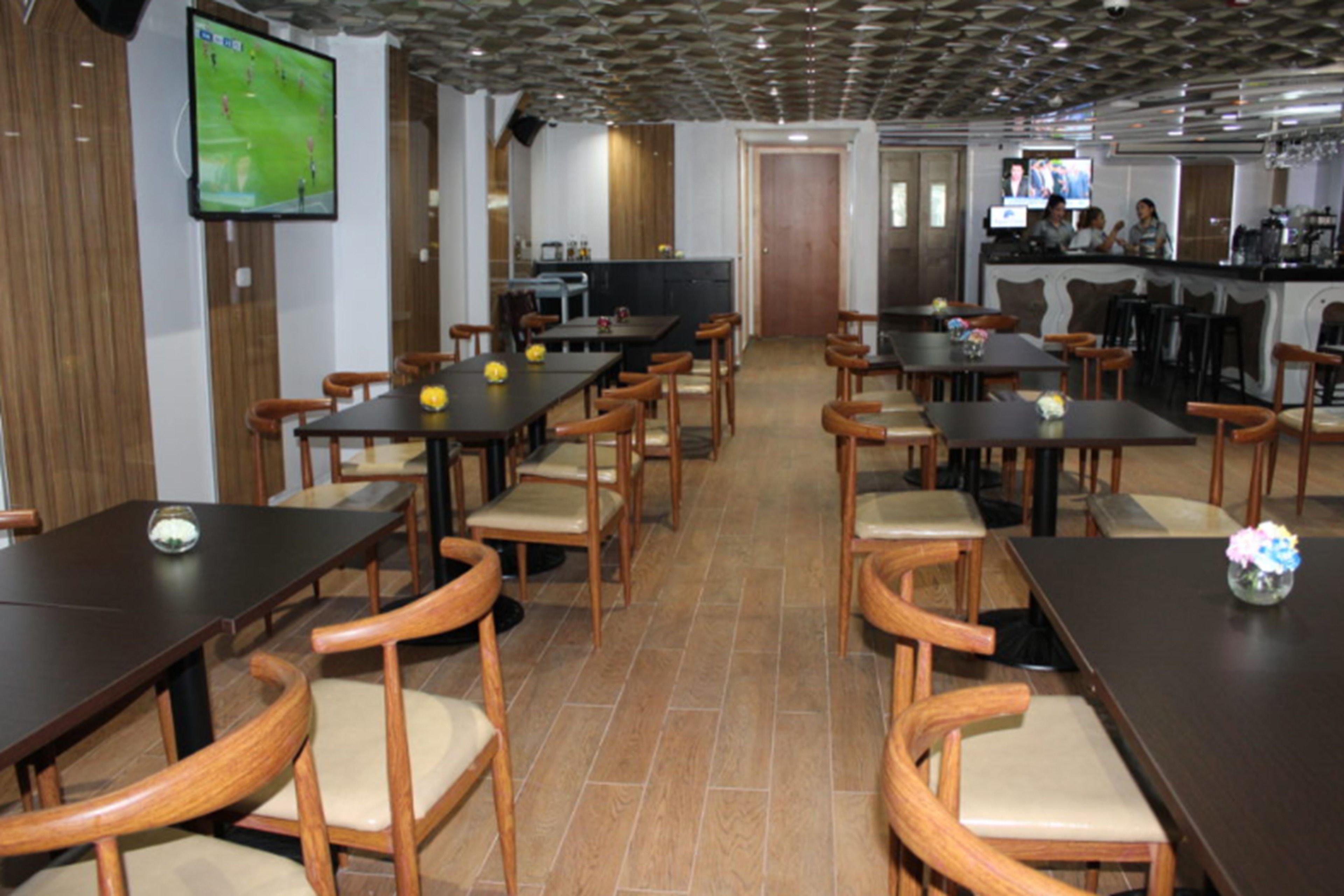 A restaurant with multiple tables and chairs, a bar area, and a television screen displaying a sports game.