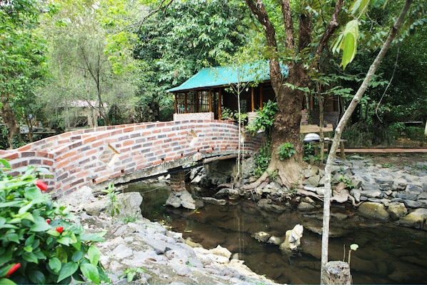 A brick bridge over a stream with a gazebo-like structure on the right.