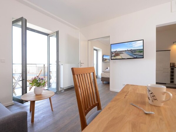 A modern living room with a wooden dining table, a coffee mug, and a TV mounted on the wall. - Ohlerich storage app. 27 (Wismar)