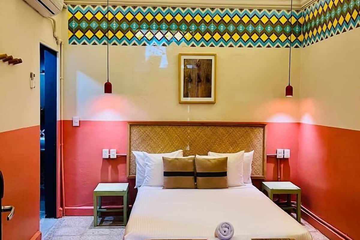 A hotel room with a bed, bedside tables, a ceiling fan, and patterned wall decor.
