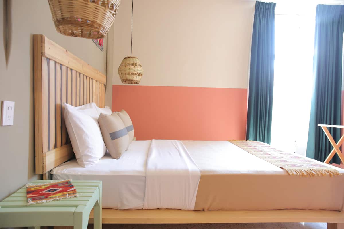 A bed with a wooden headboard, white bedding, and a small table with a colorful cloth.
